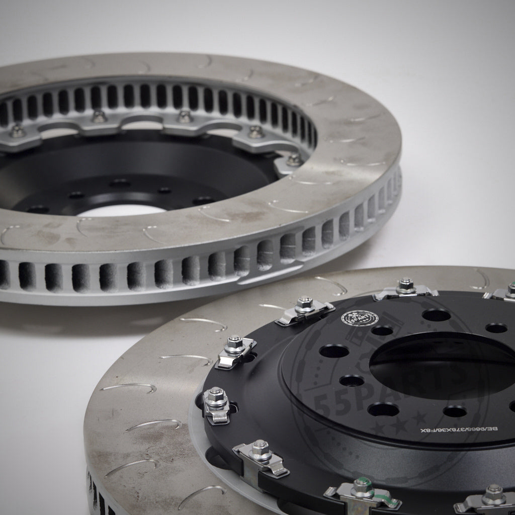 Auf einem schlichten weißen Hintergrund sind zwei 55Parts Special Aftermarket Ersatz-Reibringe J-Hook-Bremsscheiben für AP Racing-Systeme abgebildet, mit einem geschlitzten Design für verbesserte Leistung auf der Rennstrecke.