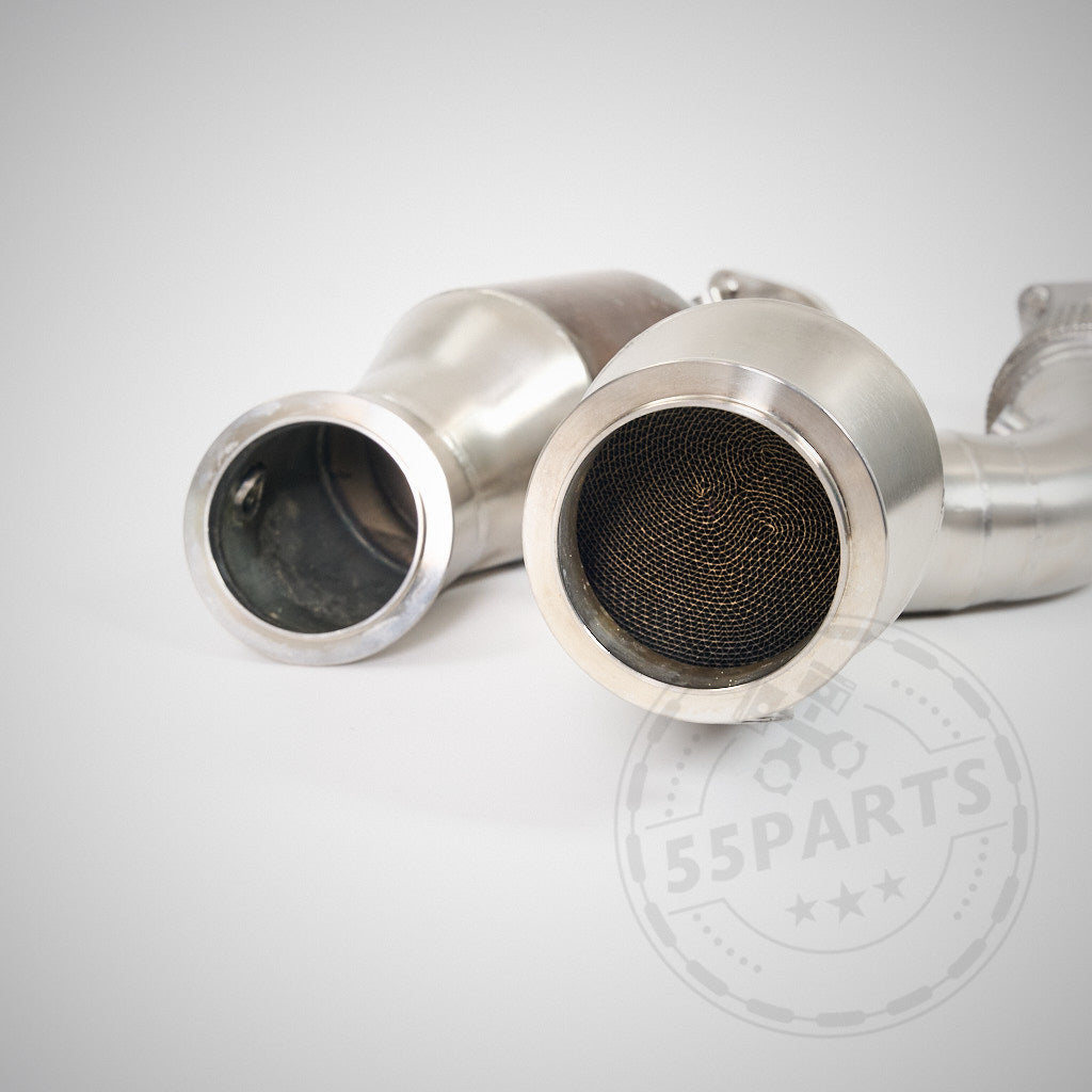 Zwei metallische High Flow Downpipes (mit 200 Zeller Euro 6 Katalysatoren) von 55Parts & MH Pipes, kompatibel mit BMW G87 M2, G80 M3 und G82 M4 S58, sind auf einer weißen Oberfläche abgebildet und verfügen über sichtbare Mesh-Innenseiten für optimalen Durchfluss.