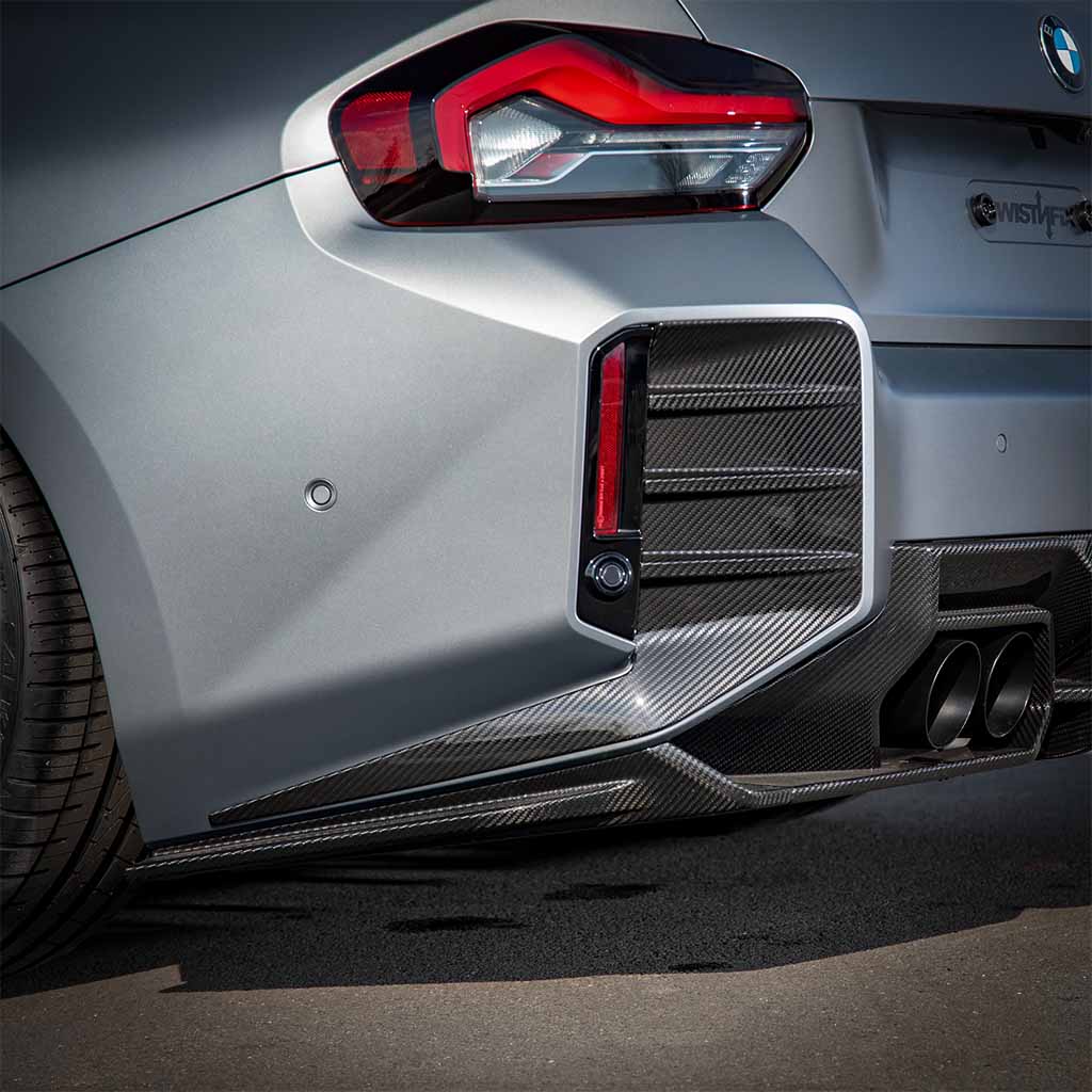Nahaufnahme eines silbernen Autos mit Twistnfix TNF+ Einsätze für Heckstoßstange Carbon, passend für BMW M2 (G87) inkl. Teilgutachten. Teilgutachten, mit Carbon-Details und Doppelauspuffrohren.