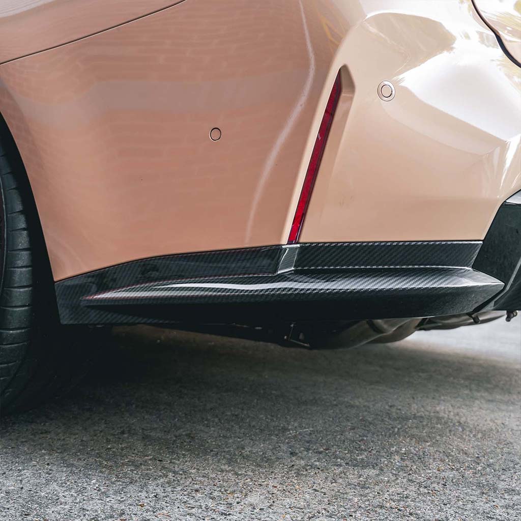 Nahaufnahme der Heckstoßstange eines Fahrzeugs mit TNF+ Heck Seitendiffusoren Carbon von Twistnfix, passend für BMW M3 (G80/G81) inkl. Teilgutachten. Teilegutachten, mit Prepreg-Carbon-Seitenschweller und vertikalem roten Reflektor.