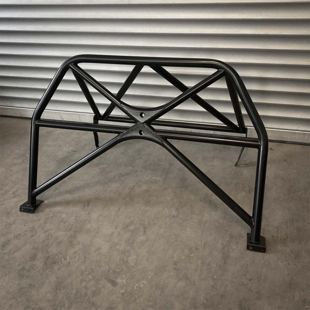Der Teutsche Clubsportbügel, passend für BMW E81/E82 inkl. Materialzertifikat, wird in schwarzem Metall mit Querverstrebung gezeigt, aufgestellt auf einem Betonboden vor einer Metallschalung.