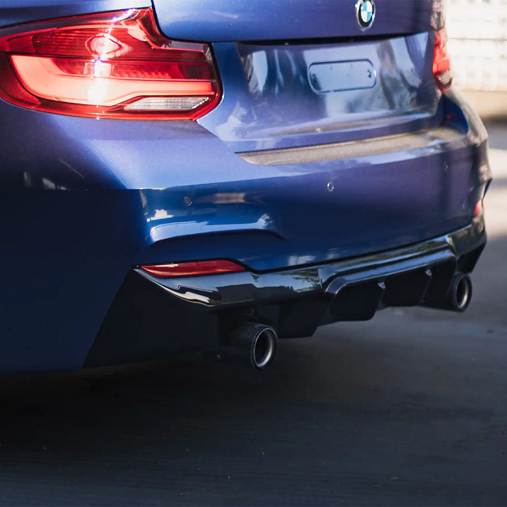 Nahaufnahme des Heckstoßfängers, ZAERO Design EVO-1 Diffusor für BMW F22, F23 M235i, M240i von ZAERO, mit Doppelauspuff an einem blauen Auto, das auf einer sonnenbeschienenen Fläche geparkt ist.