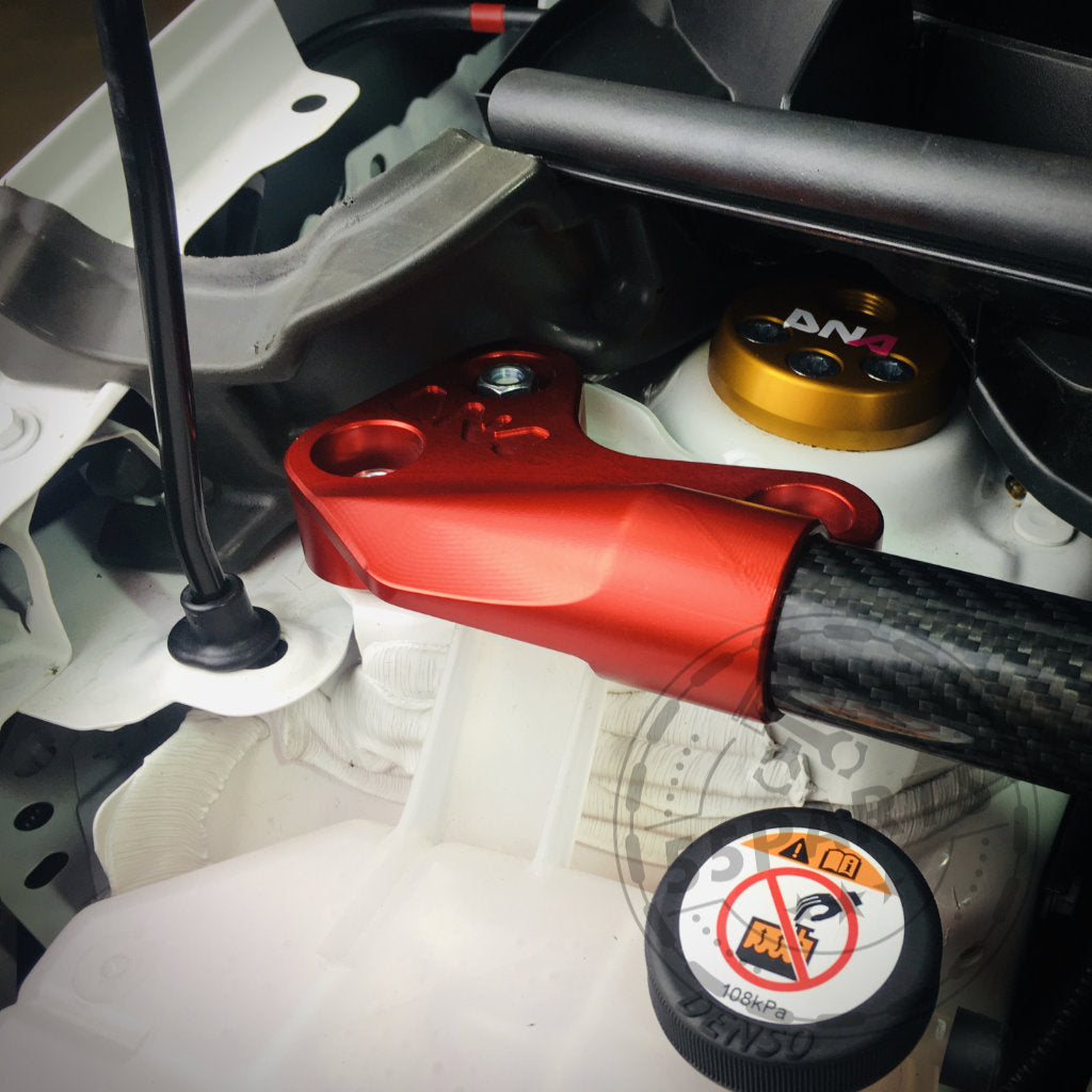 Nahaufnahme einer DNA Racing Carbon Domstrebe vorne, entworfen für den Toyota Yaris GR, eingebaut im Motorraum neben anderen Metallkomponenten.
