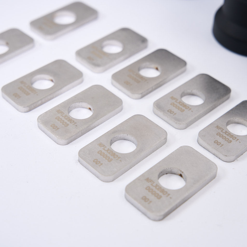 Rechteckige Metallplatten mit Mittellöchern und eingraviertem Text, inklusive 55Parts NoFlex Lager: Differential Lager (mit Höherlegung) Diff Aufhängung für BMW F8x und G8x M2, M3, M4, sind auf einer weißen Fläche angeordnet.