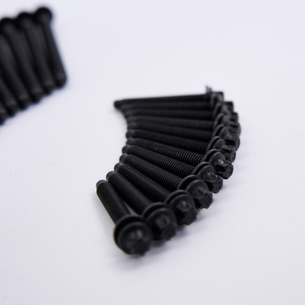 Eine geschwungene Reihe schwarzer Schrauben aus dem 55Parts Einbauset Schraubenset Injektoren passend für BMW B58 S58 ist fein säuberlich auf einer weißen Fläche angeordnet, wobei weitere Schrauben im Hintergrund verschwimmen.