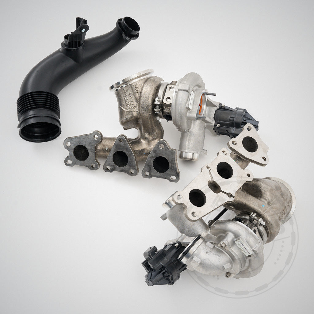 Zwei Ladermanufaktur Upgrade Turbolader LM700-LM900 Turbolader passend für BMW F80, F82, F87 M2C, M3, M4 mit S55-Motor und ein schwarzes Kunststoff-Autoteil auf hellem Hintergrund mit einem 55Parts-Wasserzeichen.