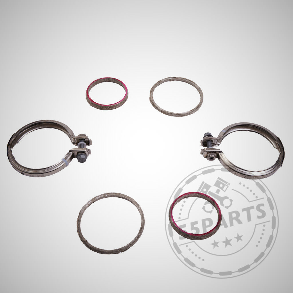 Zwei Metallklammern und vier BMW-Dichtungen aus dem Einbauset Downpipe für M2 G87, M3 G80/G81 und M4 G82/G83 mit S58-Motor, angeordnet auf hellem Hintergrund mit dezentem Logo-Wasserzeichen.