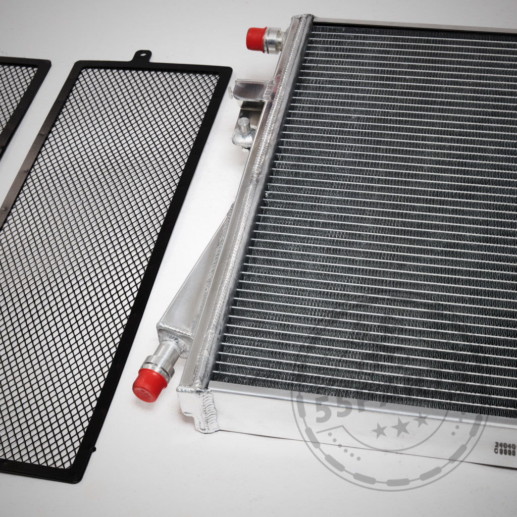Ein Autokühler aus Metall und zwei schwarze Maschensiebe auf weißem Hintergrund, mit dem 55Parts Upgrade Kühlmittelkühler Wasserkühler für BMW G8X M2, M3, M4 mit S58 Motor (inkl. Teilegutachten) für verbesserte Ladeluftkreislaufleistung.