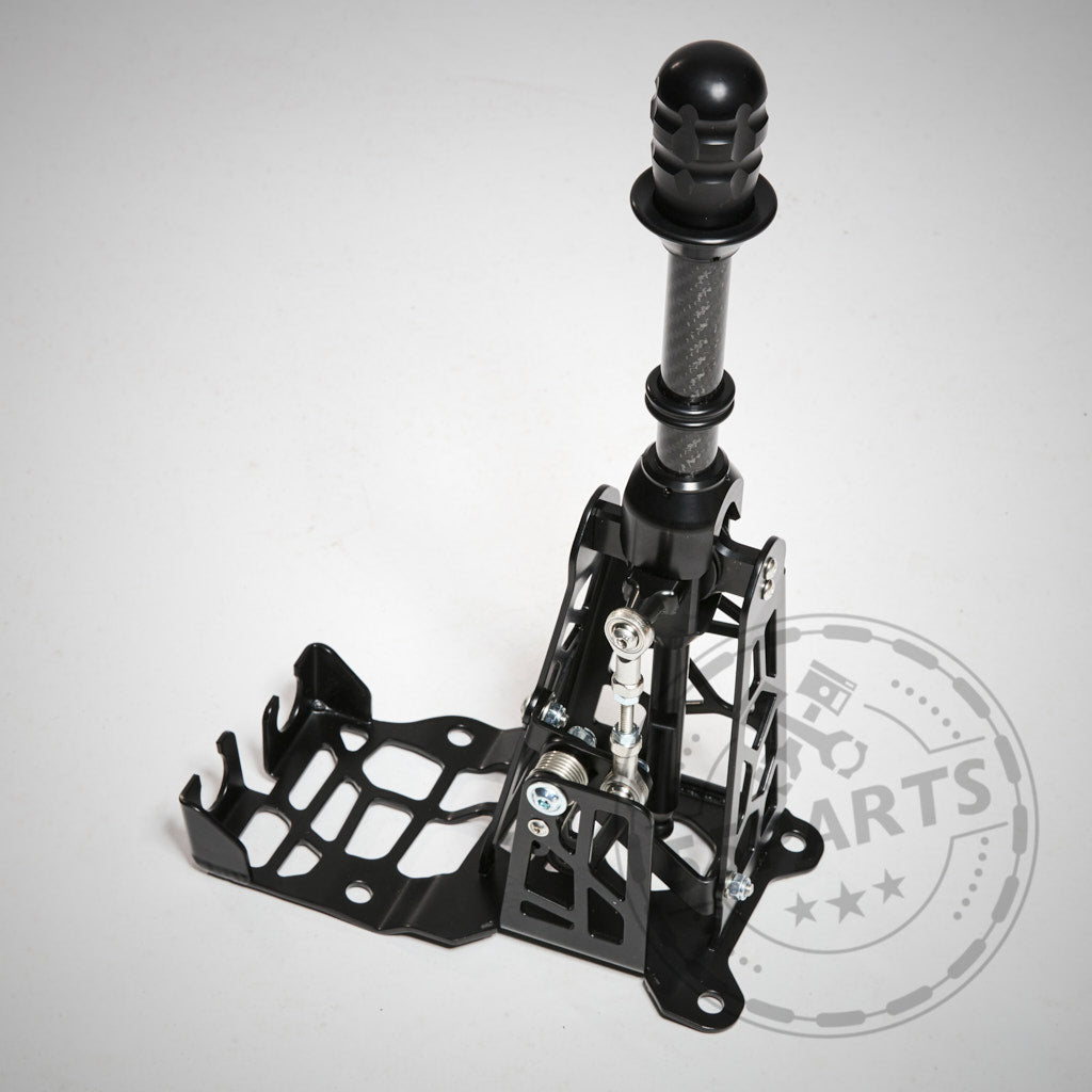 Der HRE Shortshifter passend für GR Yaris von HRE besteht aus schwarzem Metall mit einem Gittermuster auf weißem Hintergrund und ist für Seilzugschaltungen konzipiert.