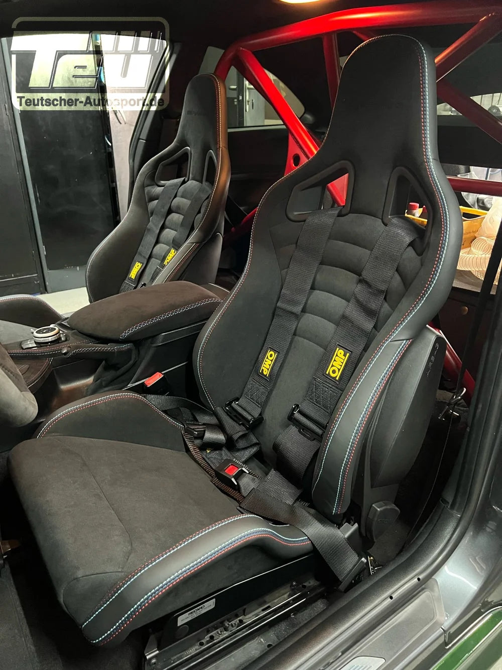 Zwei schwarze Rennsitze mit Gurten und roten Überrollbügeln sind auf Teutscher Recaro Sportster CS Sitzkonsolen montiert, passend für BMW E-, F-, G-Serie und Toyota Supra A90, komplett mit Materialzeugnis.