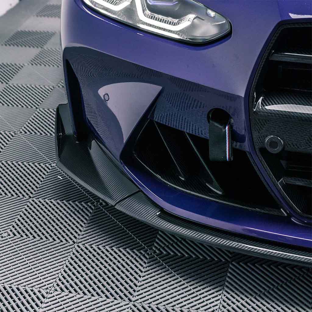 Nahaufnahme der vorderen Stoßstange und des Scheinwerfers eines blauen Sportwagens mit dem Twistnfix TNF+ CSL-Style Frontspoiler Carbon für BMW M3 (G80/G81) &amp; M4 (G82/G83), inkl. Teilgutachten. Teilgutachten, abgebildet auf einer Strukturmatte.