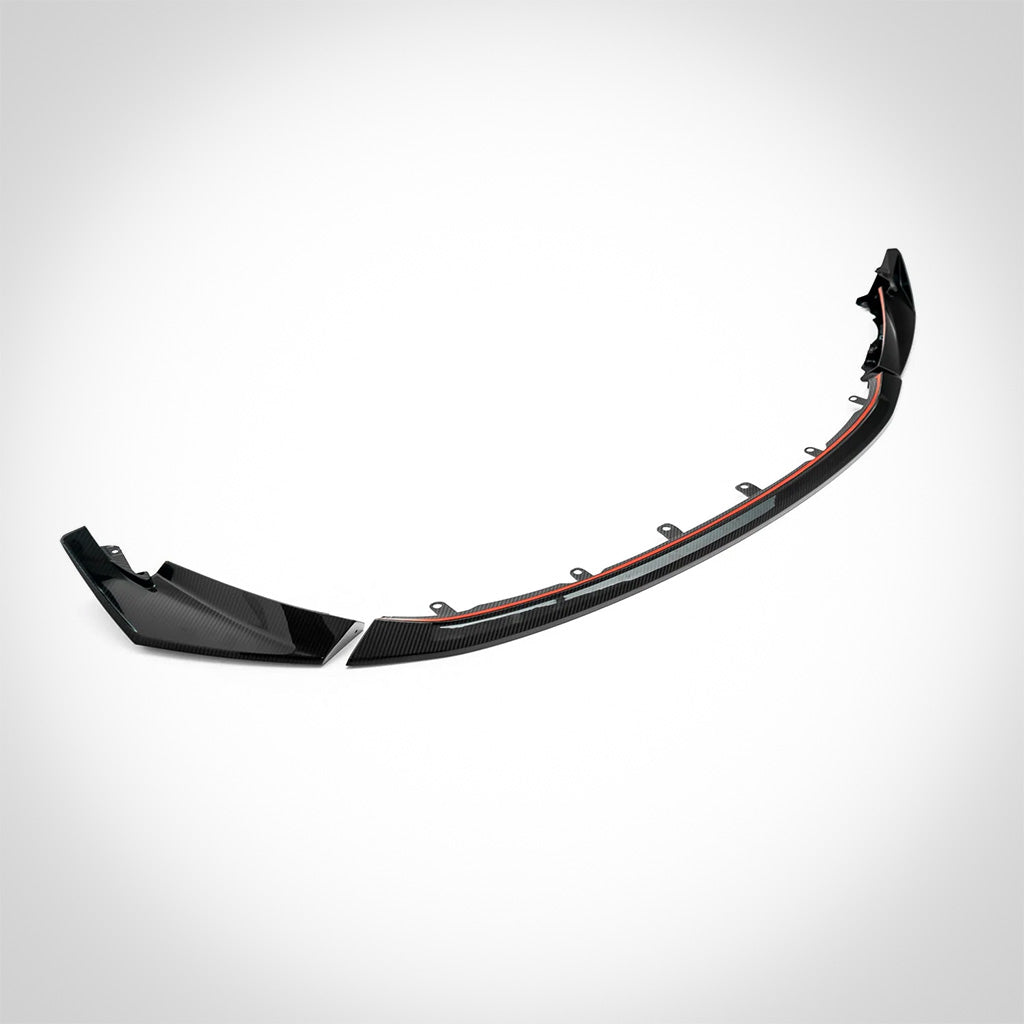Der Twistnfix TNF+ CSL-Style Frontspoiler Carbon für BMW M3 (G80/G81) &amp; M4 (G82/G83), incl. Teilegutachten, verfügt über ein geschwungenes schwarzes Design mit rotem Akzent in Prepreg-Carbonfaser, dargestellt auf weiß-ideal für die Aufwertung Ihrer Frontpartie.