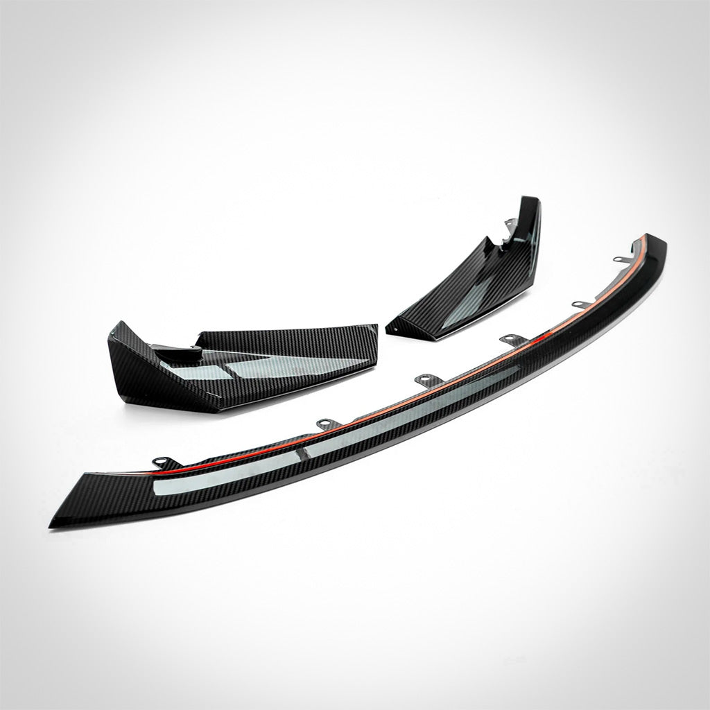 Der Twistnfix TNF+ CSL-Style Frontspoiler Carbon für BMW M3 (G80/G81) und M4 (G82/G83) incl. Teilegutachten wird in schwarzer Prepreg-Kohlefaser mit drei Karosserie-Kit-Teilen auf weißem Hintergrund gezeigt.