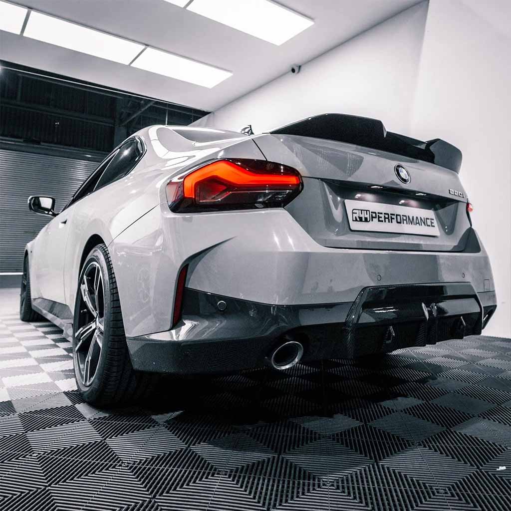 Silberner Sportwagen mit schwarzen Akzenten, geparkt in einer Halle auf einem gemusterten Boden, mit einem Twistnfix TNF+ Performance Carbon Ducktail für BMW M2 (G87) 2er (G42), inklusive Teilegutachten.