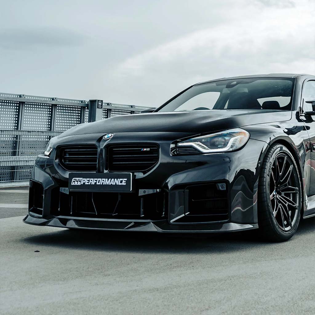 Ein schwarzer BMW M2 (G87) mit Twistnfix MHC TNF+ Edition 1 Frontspoiler Carbon, Custom Bodykit und HYPERFORMANCE Kennzeichen, geparkt im Freien - Frontansicht.