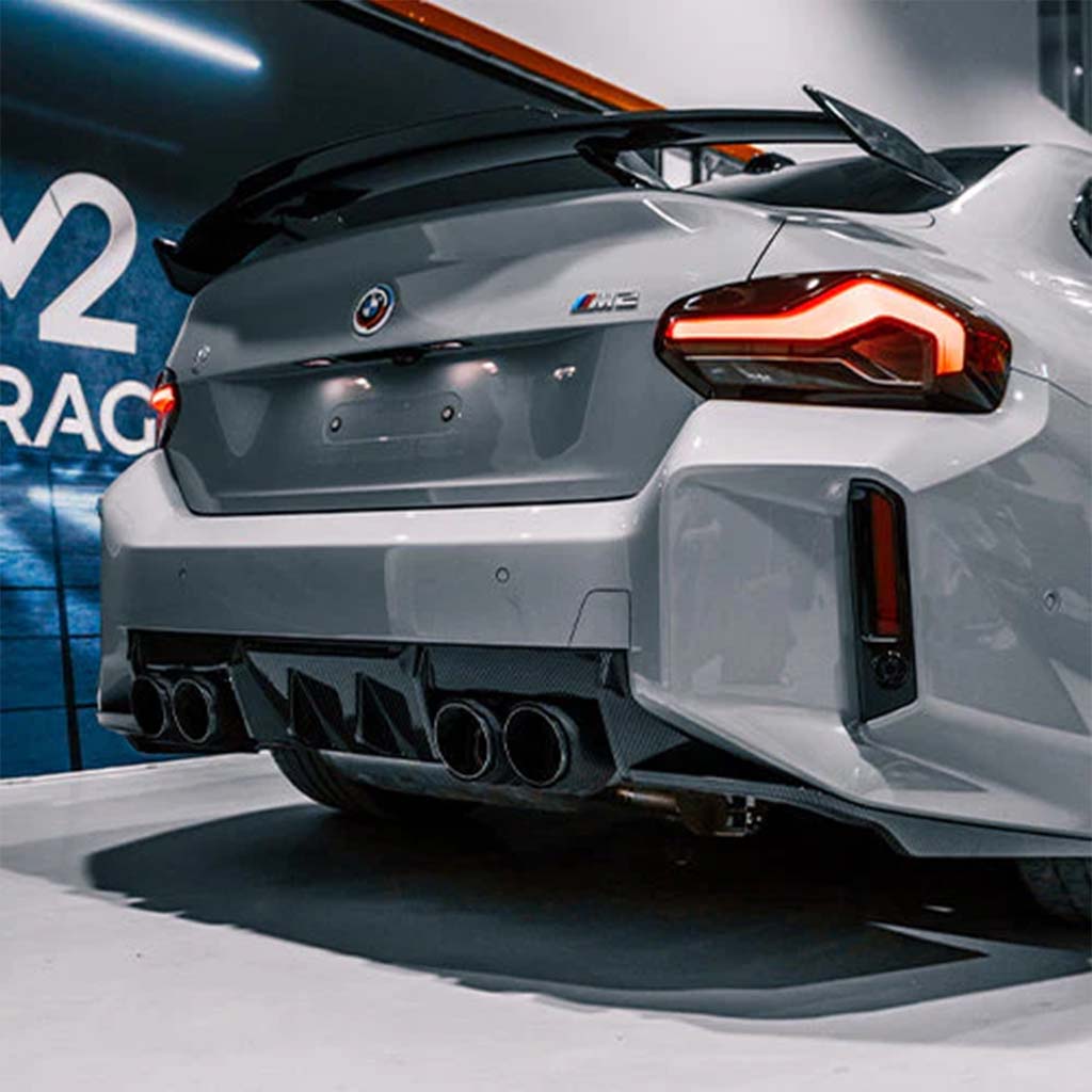 Heckansicht eines weißen BMW M2 (G87) mit OEM-Heckspoiler und Vierfach-Auspuffanlage, bestückt mit einem Twistnfix MHC TNF+ Edition 1 Heckdiffusor Carbon inkl. Teilegutachten, geparkt im Innenraum.
