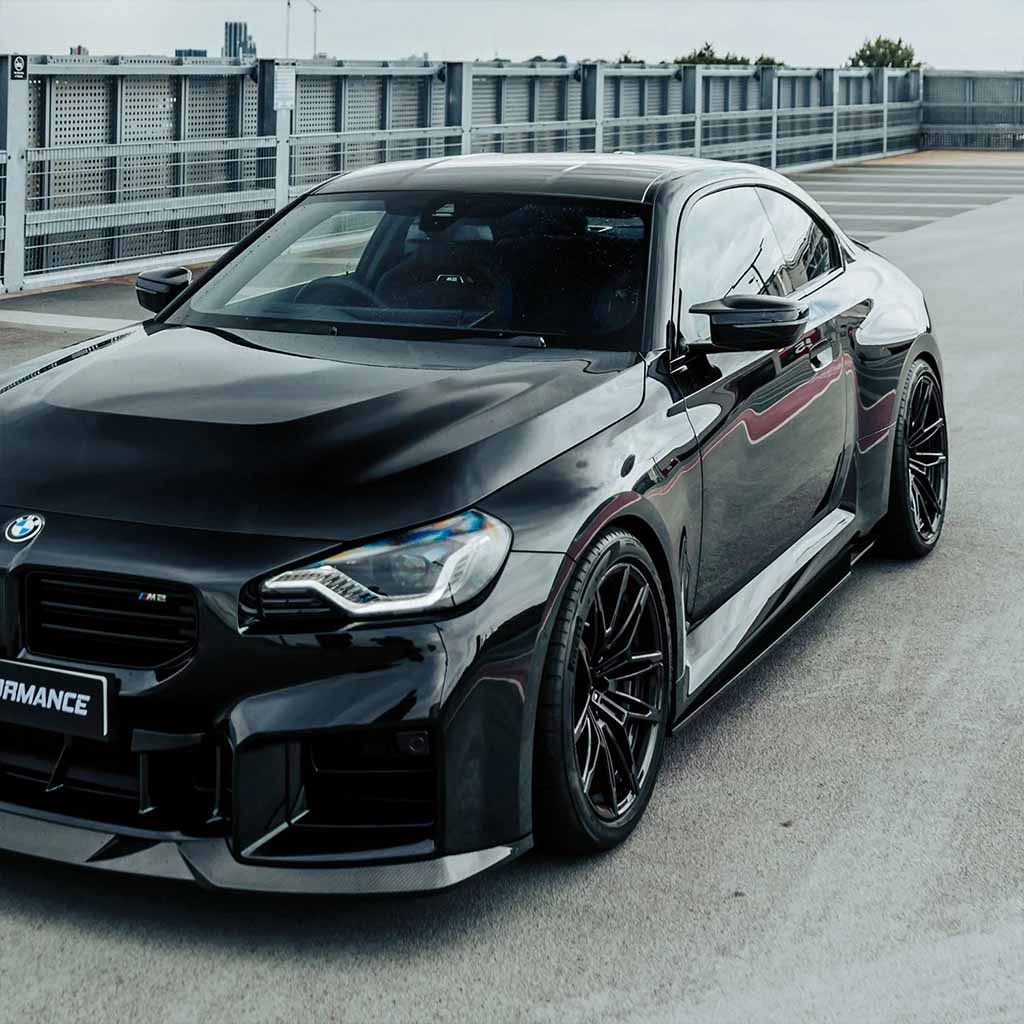 Ein schnittiger schwarzer BMW M2 (G87) mit Twistnfix MHC TNF+ Edition 1 Seitenschweller Carbon inkl. Teilgutachten steht bei Tageslicht auf dem Dach. Teilegutachten ist bei Tageslicht auf einem Dach geparkt.