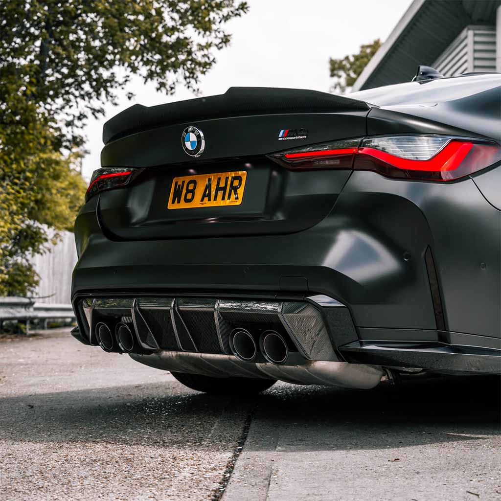 Heckansicht eines schwarzen BMW M4 (G82) mit Twistnfix TNF+ PSM Carbon Ducktail, Vierfach-Auspuffanlage und gelbem Kennzeichen W8 AHR, geparkt im Freien.
