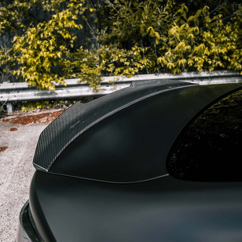 Nahaufnahme des Twistnfix TNF+ PSM Carbon Ducktail Spoilers für BMW M4 (G82)/4er (G22), geparkt in der Nähe von Grünflächen und einer Metall-Leitplanke, inklusive Teilegutachten.