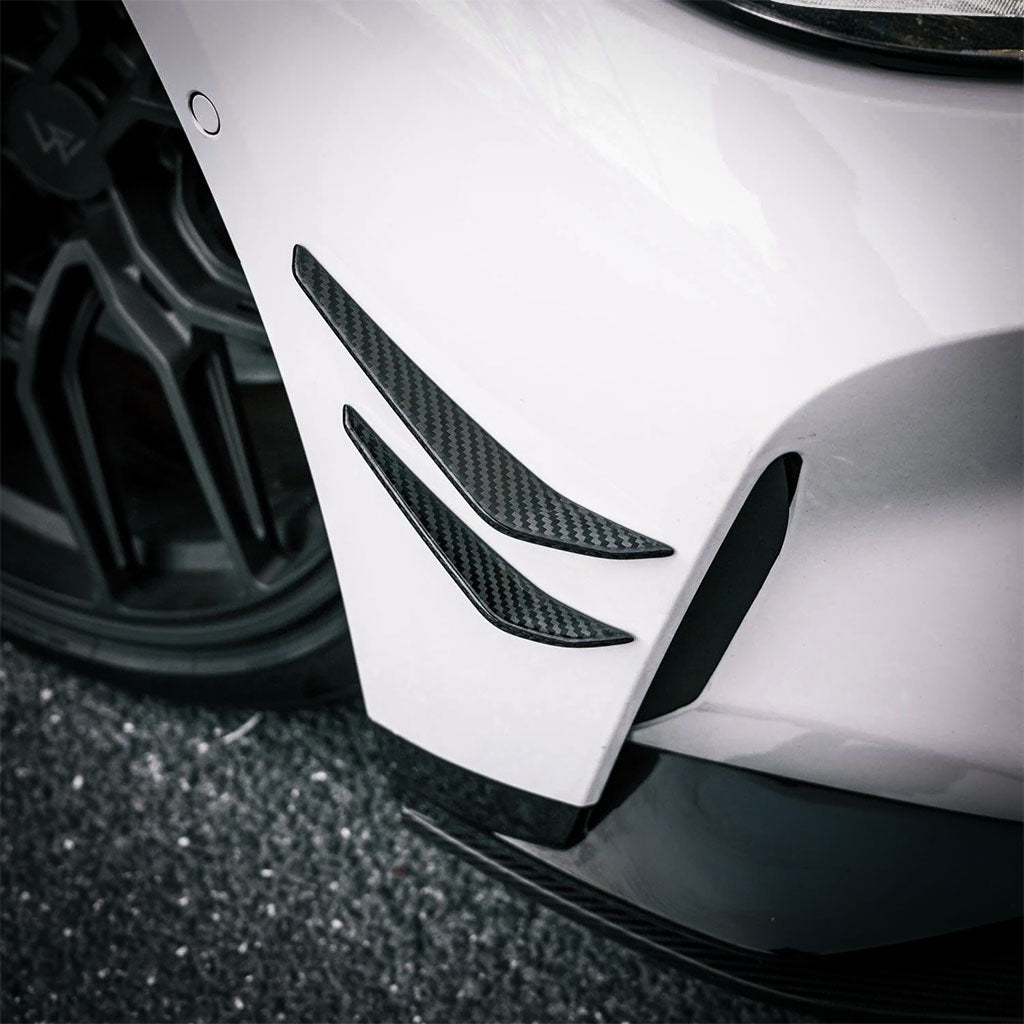 Vier schwarze Twistnfix TNF+ Performance Canards Carbon, passend für BMW M3 (G80/G81) und M4 (G82/G83), inkl. Teilegutachten, sind symmetrisch auf weißem Grund angeordnet und heben die aerodynamischen Verbesserungen hervor.