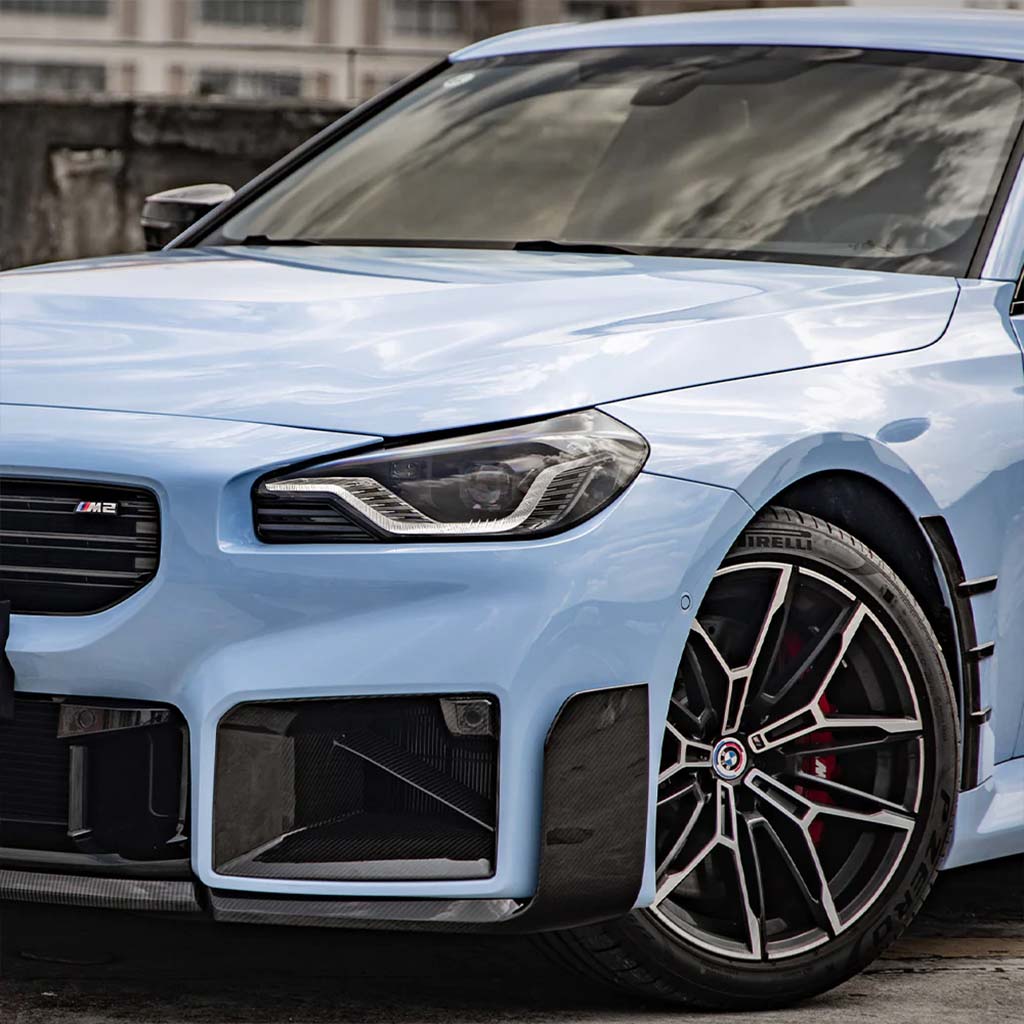Nahaufnahme eines hellblauen BMW M2 (G87) mit Scheinwerfern, Kühlergrill, Leichtmetallrädern und einem Twistnfix TNF+ Performance Frontspoiler Carbon mit Teilgutachten.