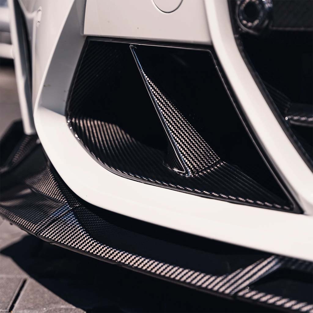 Nahaufnahme von Twistnfix TNF+ Performance Lufteinlässe Carbon für BMW M3 (G80/G81) & M4 (G82/G83), mit eleganten Kohlefaserdetails und Teilegutachten, abgebildet auf einem weiß lackierten Stoßfänger.
