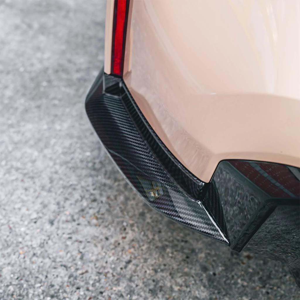 Nahaufnahme der Heckstoßstange eines Fahrzeugs mit Twistnfix TNF+ Heck Seitendiffusoren Carbon für BMW M3 (G80/G81) inkl. Teilgutachten. Teilegutachten, inspiriert von den M3 G80 Diffusoren, dargestellt auf einer strukturierten grauen Oberfläche.