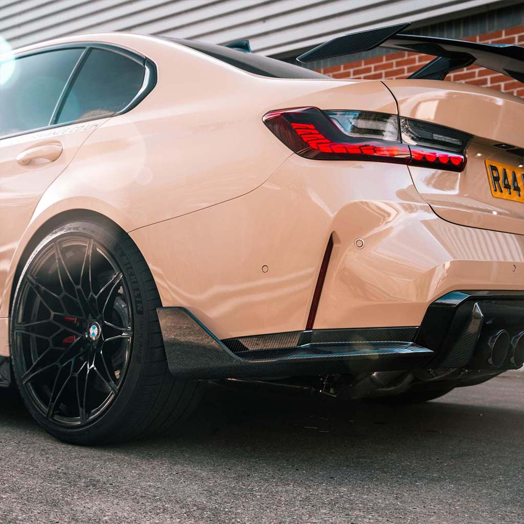 Nahaufnahme des Hecks eines beigen Sportwagens mit schwarzen Felgen, Prepreg-Carbon Spoiler und Twistnfix TNF+ Performance Seitendiffusoren Carbon für BMW M3 (G80/G81), der im Freien geparkt ist - und einen mutigen Performance-Stil unterstreicht.
