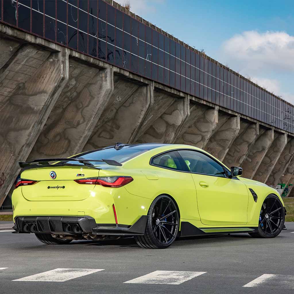 Ein lindgrüner BMW M3 (G80/G81) ausgestattet mit Twistnfix TNF+ Performance Seitenschweller Carbon inkl. Teilgutachten. Teilegutachten ist in der Nähe einer großen Betonstruktur geparkt, Seitenansicht hinten.