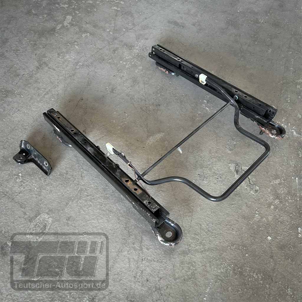 Teutscher Recaro, Sparco, OMP Sitzkonsolen passend für Ford Fiesta MK.7 incl. Materialnachweis liegen als schwarze Metallschienen und Halterungen auf einem grauen Betonboden mit dezentem Logo in der Ecke.
