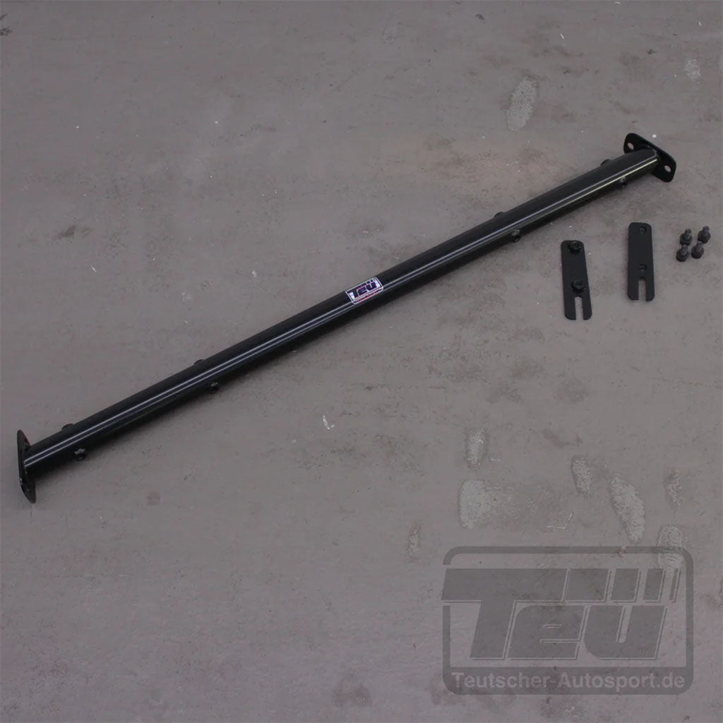 Schwarze Metallstrebe mit Halterungen und Schrauben auf grauer Oberfläche. Die Teutscher Trackday Gurtstrebe für 4-Punkt Gurte passt für den BMW G87 M2 und wird inklusive Materialgutachten geliefert. Plug'n'Play-Installation für Enthusiasten.