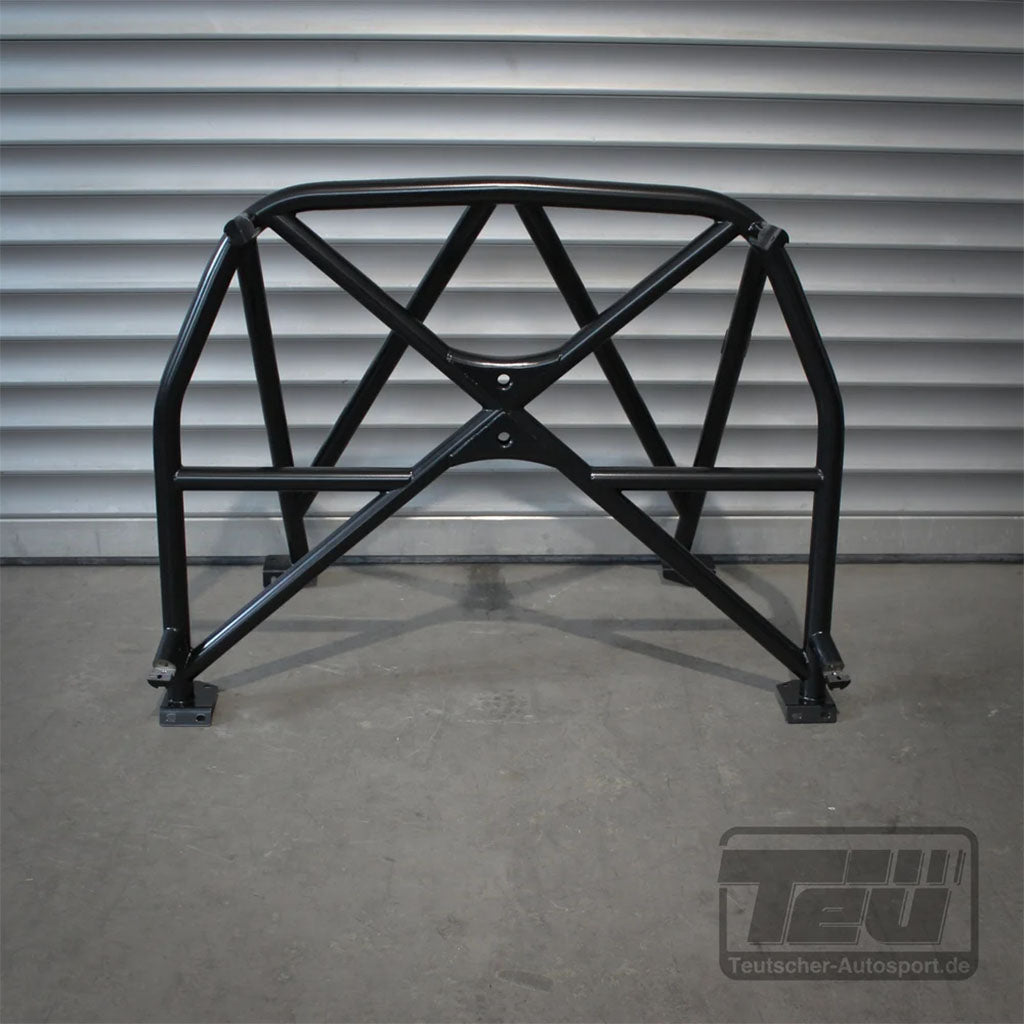 Der Teutscher Clubsportbügel für Mini R50/R53 (inkl. Materialzeugnis) ist ein schwarzer Überrollbügel aus Metall mit Querverstrebung, der auf einem Betonboden vor einer Metallwand steht.