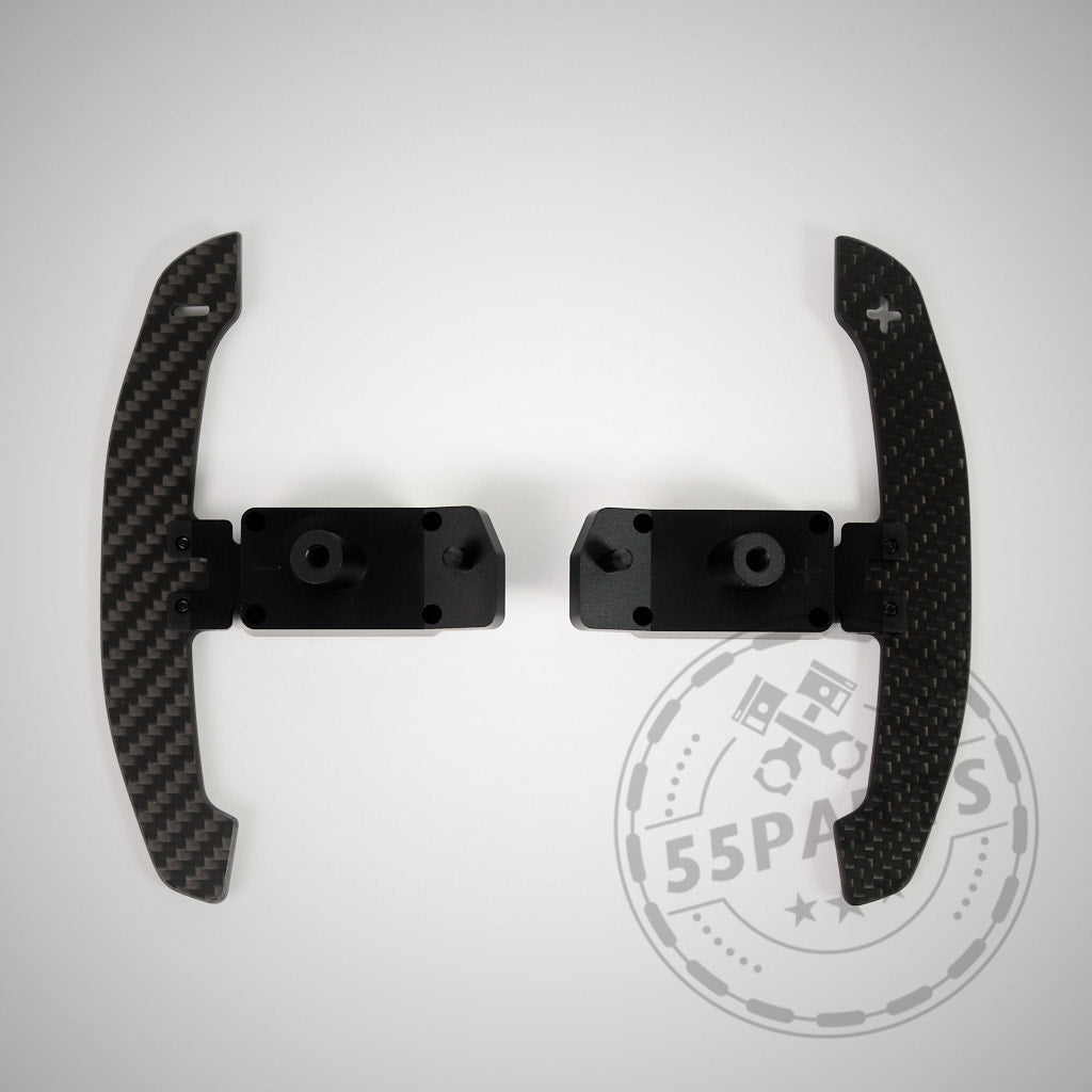 Die 55Parts Special magnetischen Schaltwippen (Kohlefaser) für den Toyota GR Yaris, hier mit schwarzen Halterungen auf hellem Grund, sorgen für echtes Rennsportfeeling. 55Parts Logo sichtbar.