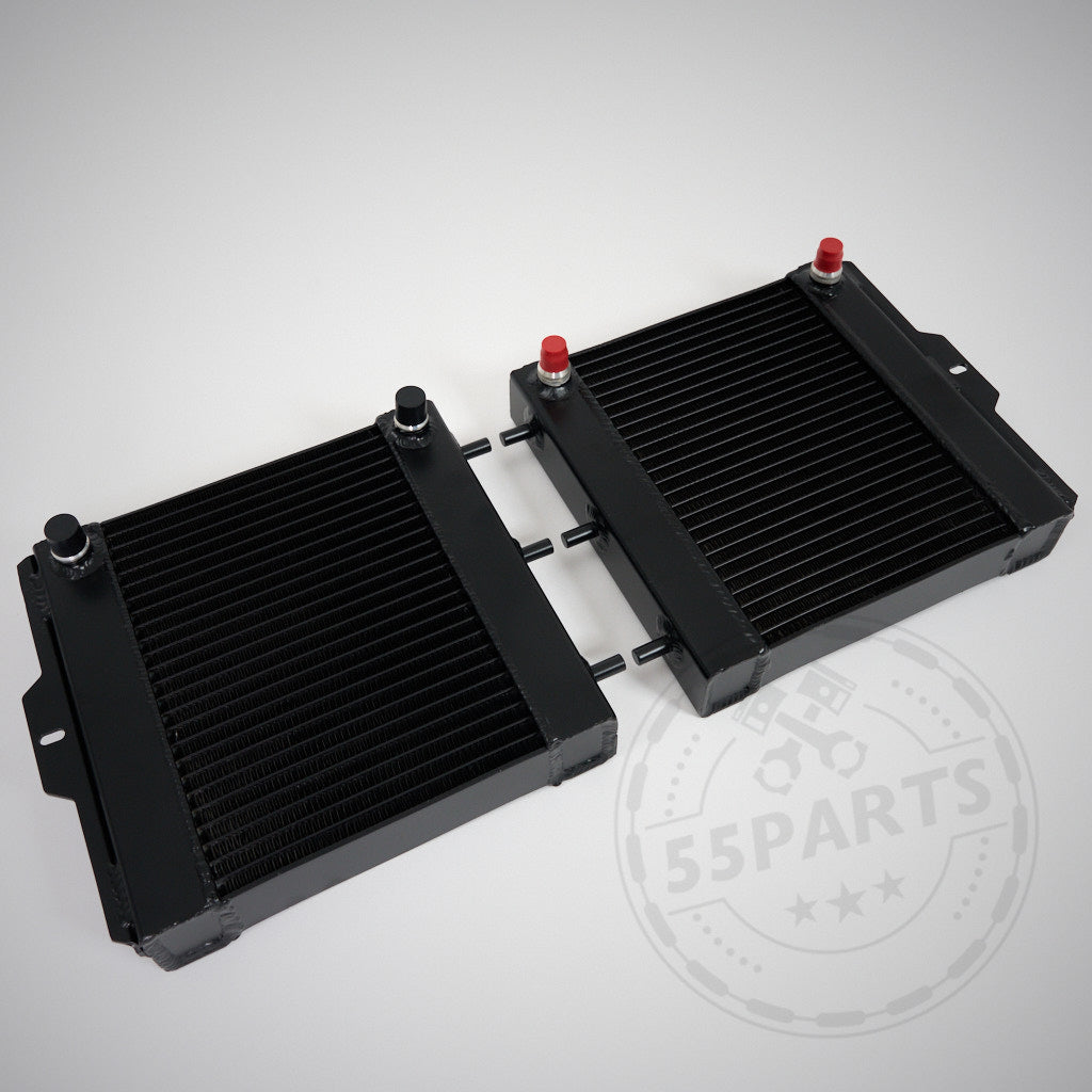 Zwei schwarze 55Parts Aluminium-Upgrade-Kühlmittelkühler, Wasserkühler seitlich (passend für BMW M2 Competition, M3, M4 F8x S55) mit Metalllamellen und rot/schwarzen Kappen, nebeneinander auf einer hellen Oberfläche platziert.
