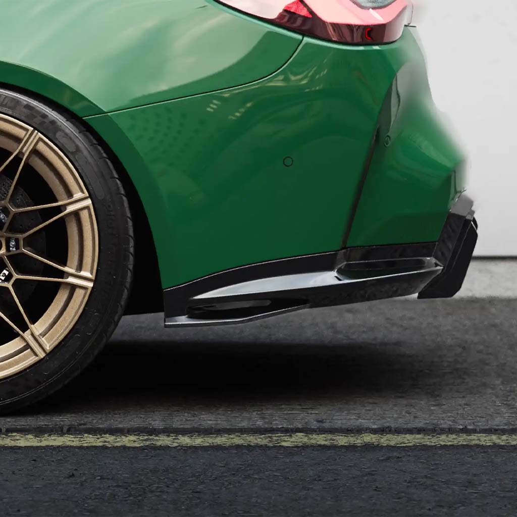 Nahaufnahme des Hinterrads und der Stoßstange eines grünen Autos mit einem ZAERO Design EVO-S Diffusor Erweiterung für BMW M4 G82/G83, geparkt an einem Bordstein auf einer asphaltierten Straße.