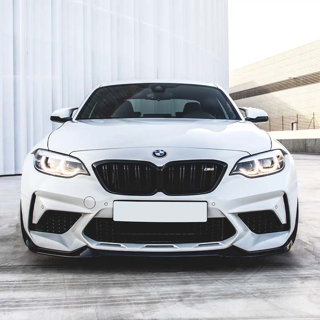 Frontansicht eines weißen BMW F87 Competition mit einer ZAERO Design EVO-S Frontlippe von ZAERO, geparkt im Freien in einer modernen, minimalistischen Umgebung.