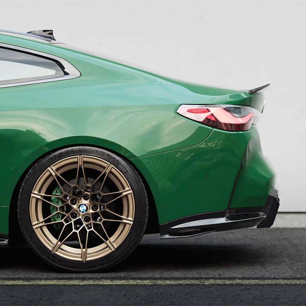 Nahaufnahme des Hecks eines grünen BMW M4 G82 mit goldenen Leichtmetallrädern und einem ZAERO Design EVO-S Heckspoiler, geparkt auf einer Straße.