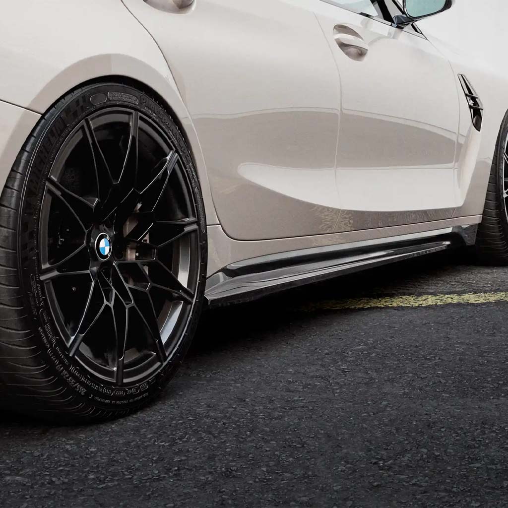Nahaufnahme eines weißen BMW M3 G80 mit ZAERO Design EVO-S Seitenschweller und schwarzem OEM+ Design Leichtmetallrad, geparkt auf Asphalt.