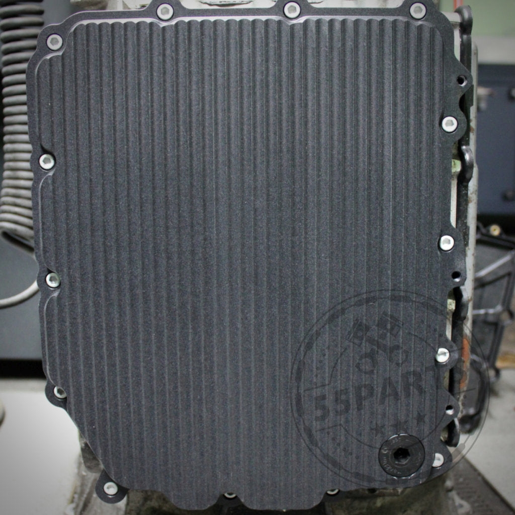 Nahaufnahme einer gerippten, rechteckigen 55Parts Exclusive Aluminium-Ölwanne (DKG GS7D36BG) mit Schrauben am Rand, entworfen passend für BMW 1/335i, M2(c), M3, M4, M5 und M6 E- &amp; F-Serie.