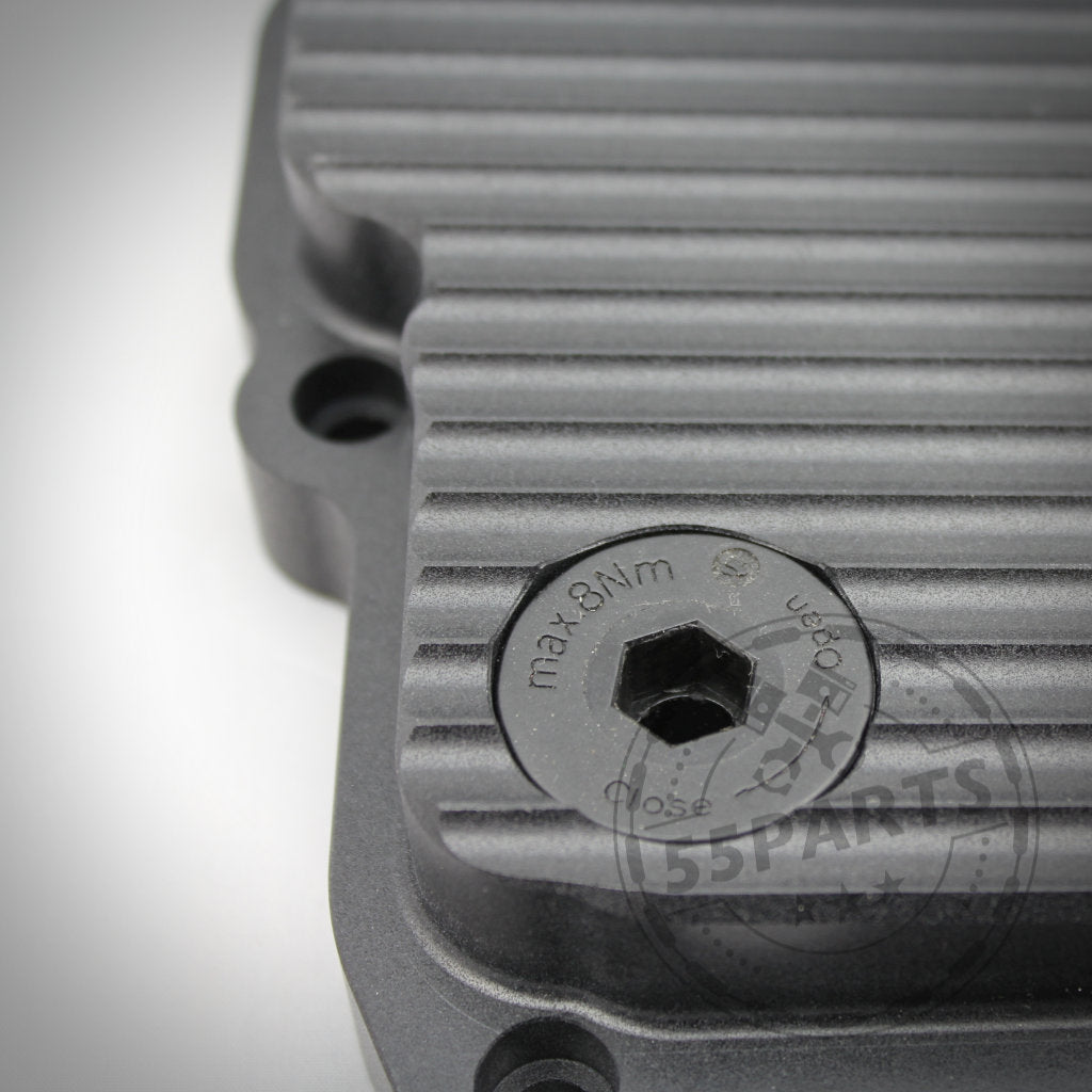 Nahaufnahme der 55Parts Exclusive DKG GS7D36BG Aluminium-Ölwanne passend für BMW 1/335i, M2(c), M3, M4, M5, M6 E- und F-Serie – mit gerippter Metallabdeckung und Sechskantschraube mit der Markierung „max. 8 Nm“ und Richtungspfeilen.
