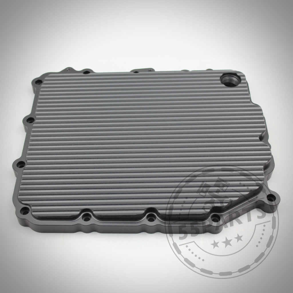 Die 55Parts Exclusive DKG GS7D36BG Aluminium-Ölwanne für die BMW 1/335i, M2(c), M3, M4, M5 und M6 E- &amp; F-Serie verfügt über ein geripptes rechteckiges Design mit Schraubenlöchern und einer runden Öffnung, dargestellt auf weißem Hintergrund.