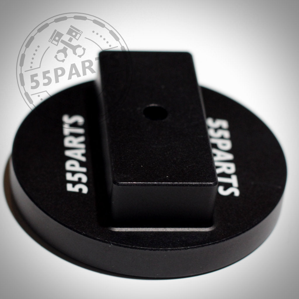 Der 55Parts Jackpad Wagenheberadapter Anhebehilfe Aufbockhilfe passend für BMW ist ein schwarzes kreisförmiges Magnetwerkzeug mit einem zentralen rechteckigen Block, ideal als CNC-gefräste Platte für Wagenheberaufnahme. Marke: 55Parts. Stellen Sie auf einen weißen Hintergrund ein.