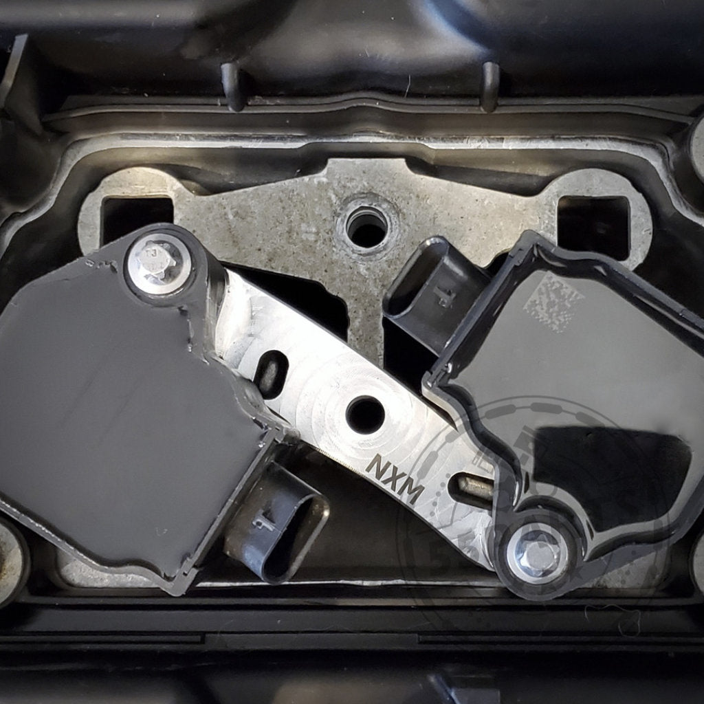 Silberne Metallhalterung mit zwei Löchern und der Gravur NXW1 auf weißem Grund. Teil des 55Parts Exclusive NexSys B58 Zündspulen Upgrade Kits passend für BMW S55 & N55 (E8x, E9x, F2x, F3x, F8x) von Nexsys Motorsport – perfekt für Tuning-Fans.
