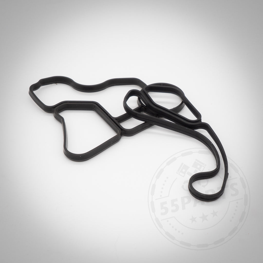 Schwarze Gummidichtung(en) Thermostatgehäuse passend für N52, N53, N54, N55 und S55 Motoren auf weißem Hintergrund mit einem schwachen kreisförmigen Logo-Wasserzeichen.