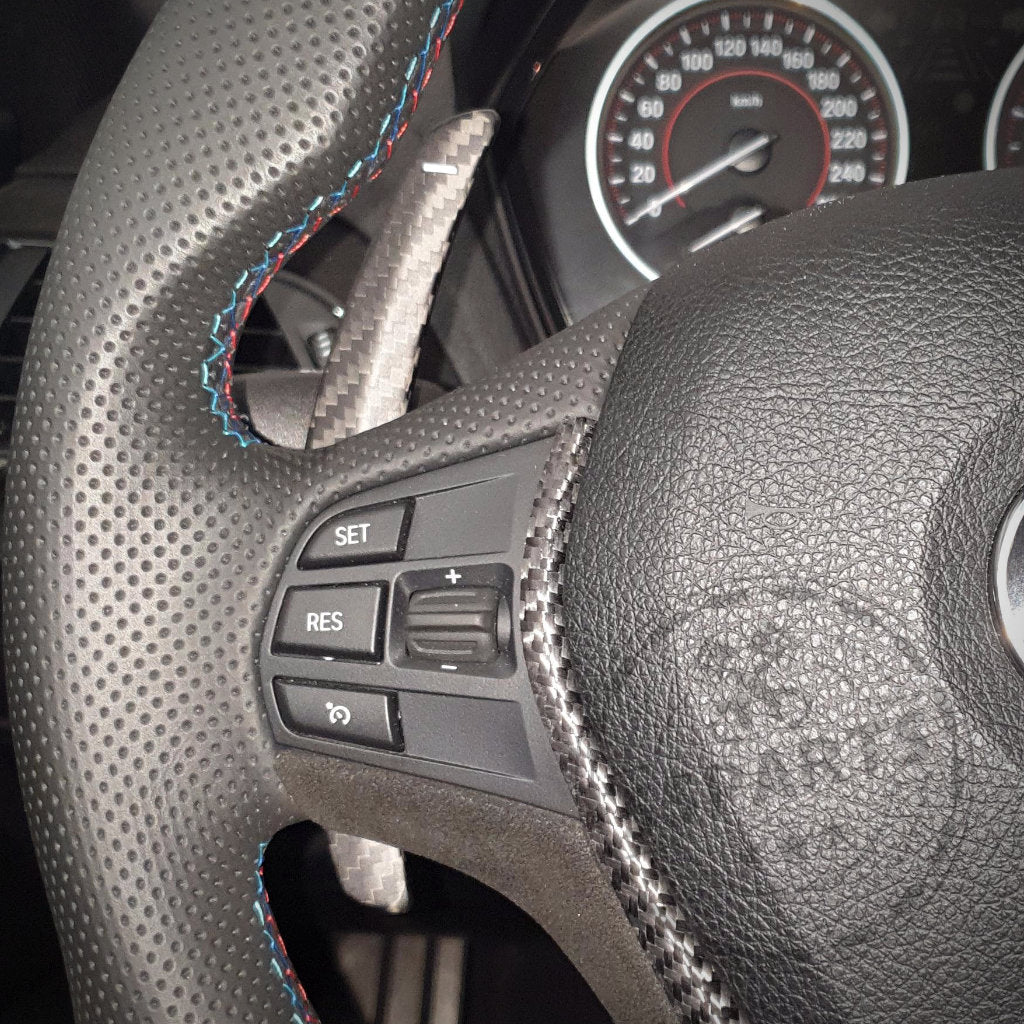 Nahaufnahme eines BMW F-Serie Lenkrads mit 55Parts Aluminium/Carbon Schaltwippen, Bedienknöpfen und einem Teil des Tachometers im Blick. Passend für BMW 1/235, 40i, 3/435, 40i, M2, M3 und M4 F-Serie.