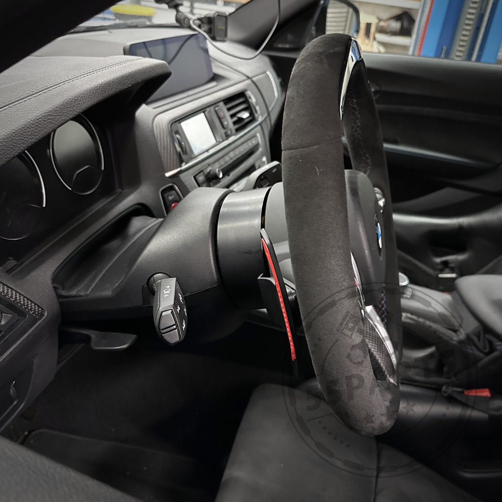 Nahaufnahme eines BMW F8X M3/M4-Lenkrads und Armaturenbretts mit Schaltwippen, Schaltknöpfen und einem DDM Racing Srls Wheel Spacer, kompatibel mit allen BMW F8X/G8X-Modellen, anderen F- &amp; G-Serien, Mini (F55/F56/F57) und Supra MK5.